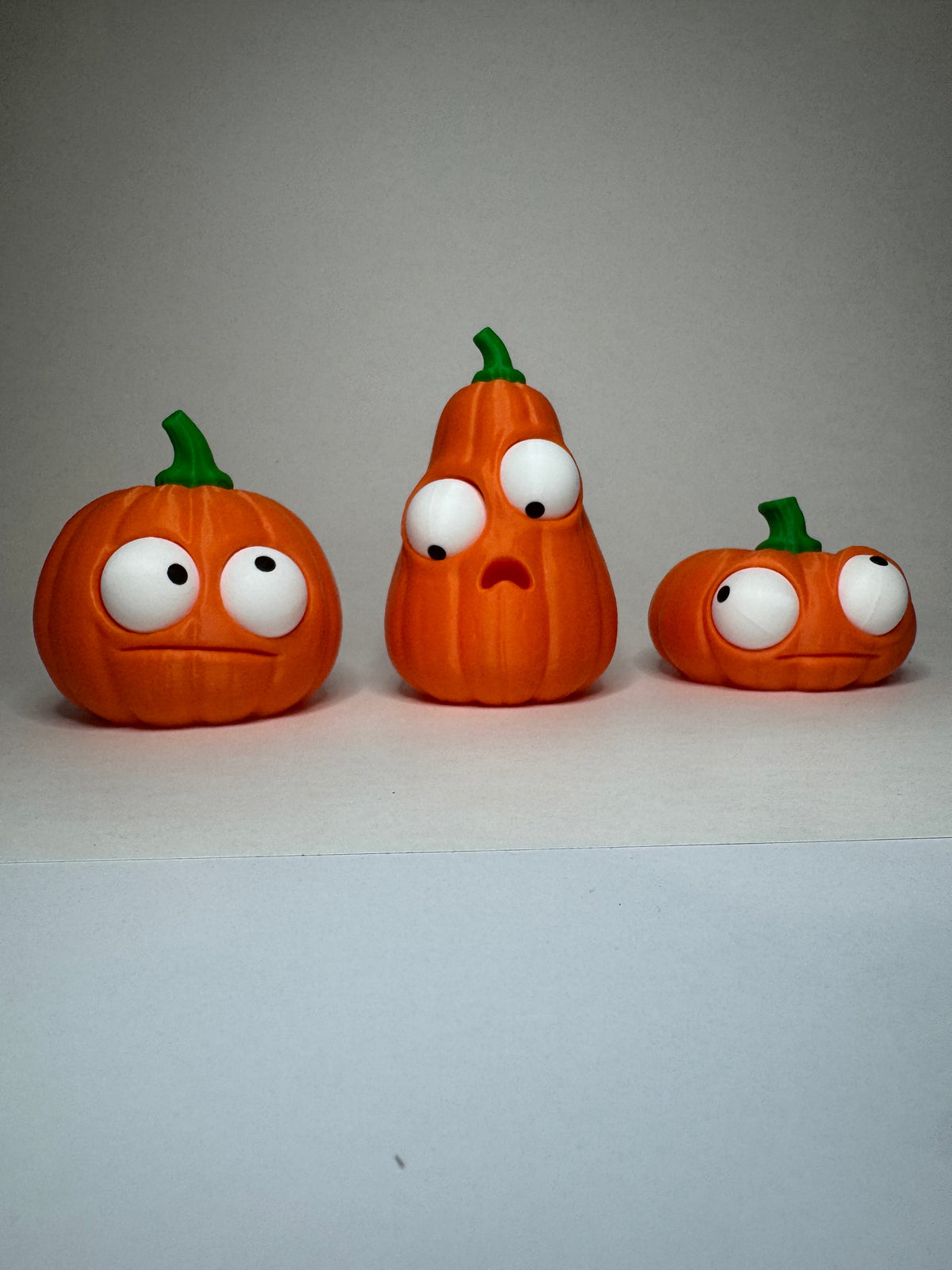 Orange Goofy Pumpkins with green stems and posable eyes, three shapes shown together